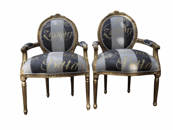 A Pair of French Style Arm Chairs Hand Gilded With Gold Leaf And Upholstered In an Imported Script Fabric