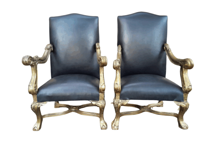 A 20th Century French Style Ornately Carved Pair Of Arm Chairs Hand Gilded And Upholstered In A Deep Buttoned Leather